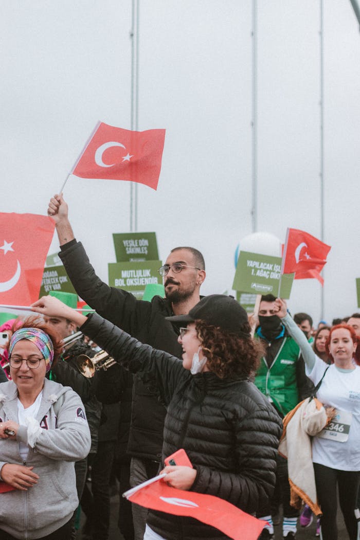 Large group rally waving Turkish flags outdoors with placards visible, showcasing cultural pride.