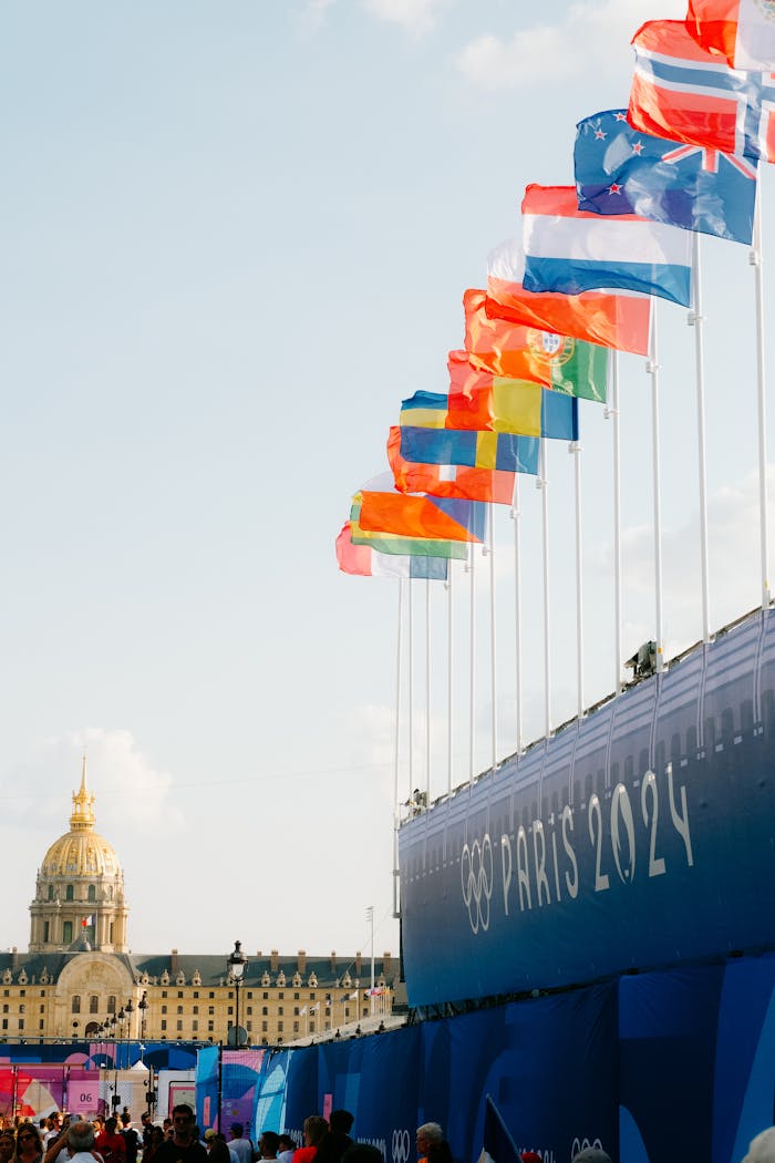 Flags of various nations at the Paris 2024 Olympics venue with a historic dome in the background.